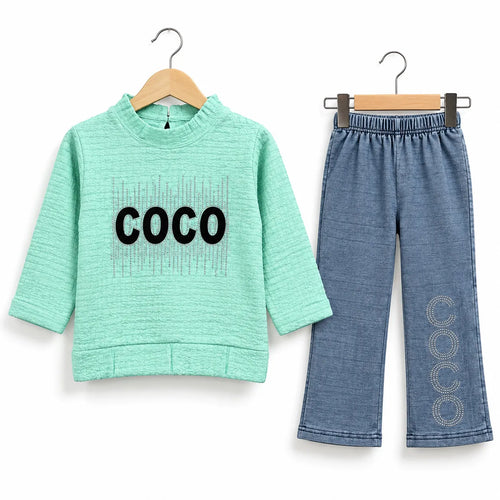 A two-piece children's outfit set on wooden hangers against a white background. The set includes a mint green long-sleeve top with 'COCO' printed in black across the chest, and a pair of blue denim-style pants with 'COCO' printed vertically in circular pattern down one leg.