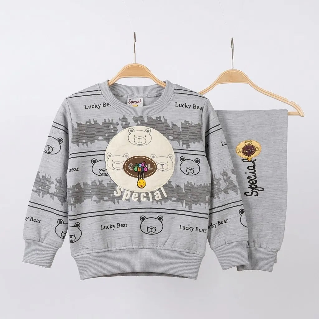 A children's two-piece sweatshirt and pants set in heather gray, hanging on wooden hangers against a light gray background. The sweatshirt features a central bear graphic with 'Cute Bear Special' text, and 'Lucky Bear' text printed all over.