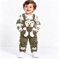 Baby boy wearing olive green teddy bear dungaree set with printed shirt