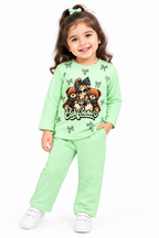 A young girl with brown hair in a ponytail wearing a mint green two-piece pajama set with a teddy bear graphic and white sneakers, standing against a plain white background.