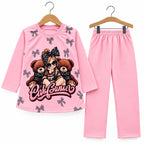 A two-piece children's pajama set on wooden hangers, featuring a long-sleeve pink top with a cartoon girl, teddy bears, and bow print, and matching pink pants.