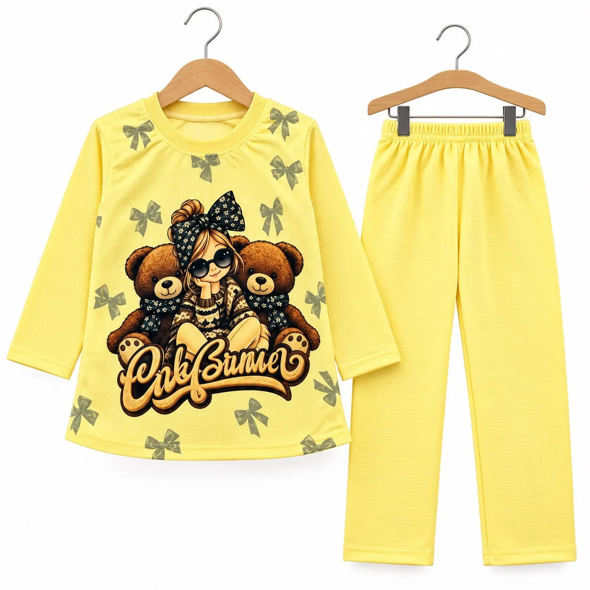 A two-piece children's pajama set consisting of a long-sleeve yellow top and matching pants, displayed on wooden hangers against a white background. The top features a graphic print of a girl with sunglasses and two teddy bears, with the text 'Only Bummer' written below, and is decorated with small green bow motifs.